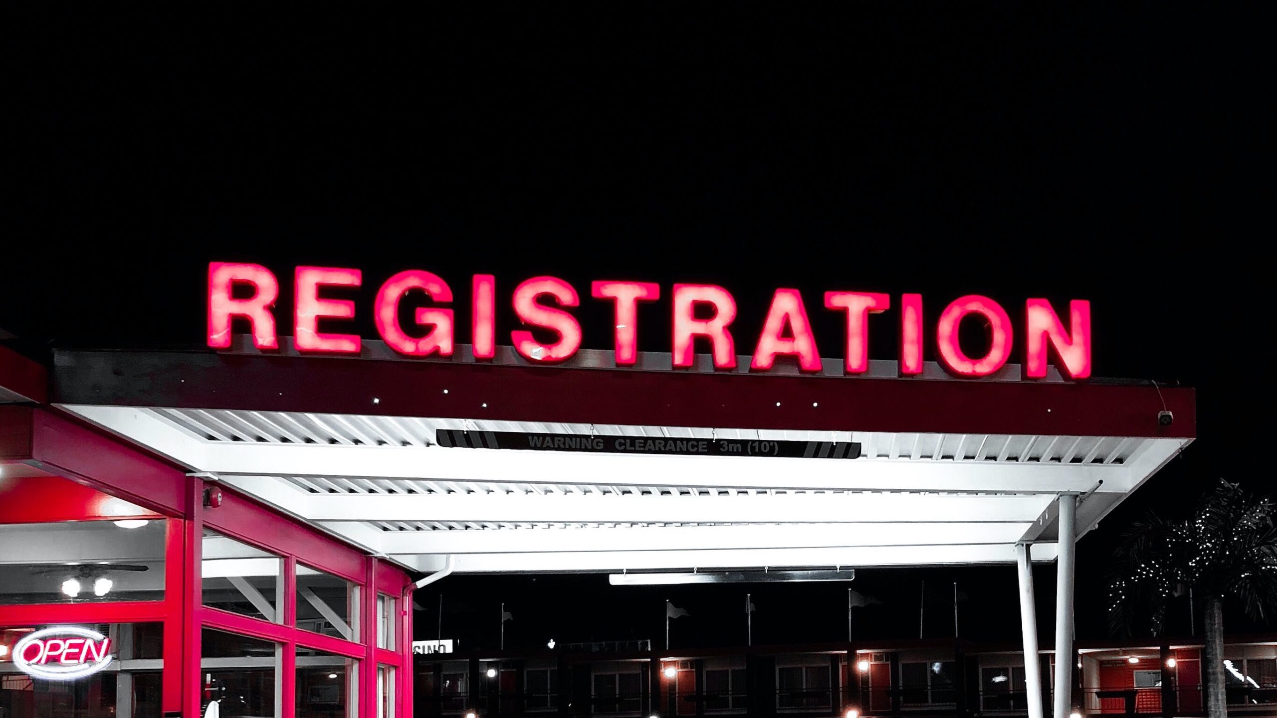 A neon sign reading "REGISTRATION" in front of a hotel at night.